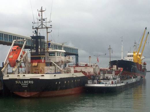 Es kam über den Elbe-Lübeck-Kanal. Am Schlepphaken ging es weiter über die Ostsee nach Rügen: Seit dem 15. Mai ist das Tankmotorschiff „Elly“ im Ostseehafen Mukran unterwegs. Wie der Hafenbetreiber meldete, bietet der Bunkerservice Friedrich G. Frommann damit nun Gasöl DMA und Diesel an. Als Kooperationspartner liefert TL Tanker Logistics weiteren Schiffsbedarf wie beispielsweise Schmieröle zu. Das 1958 in Erlenbach am Main gebaute, in Zwijndrecht behematete 80-Meter-Schiff lädt insgesamt 1.200 Tonnen in zwei Partien. Damit können Seeschiffe günstiger als zuvor, im Schichtbetrieb zu jeder Tages- und Nachtzeit sowie flexibel an verschiedenen Liegeplätzen versorgt werden. „Durch die stark ansteigende Anzahl von Schiffsanläufen ist das Bunkerschiff wichtiger denn je“, betonte Hafenchef Harm Sievers. „Vor allem Schiffe, die im Pendelverkehr zu den Offshore-Windparks im Einsatz sind, brauchen täglich neuen Treibstoff.“ Der Treibstoff kommt direkt vom Bunker-Seeschiff, was die angespannte Verkehrslage auf den Rügener Straßen entlastet: Bislang erfolgte der Nachschub über Tankwagen. Im Hafen haben Frommann und TL außerdem eine Lagerhalle für Schiffsbedarf und Schmieröle angemietet. Ausnahme für Hafengewässer Über 14 Stunden dauerte die Schleppfahrt entlang der Ostseeküste, berichtete Tim Heickmann aus dem Frommann-Team gegenüber Bonapart. Für die Transportgenehmigung des unter niederländischer Flagge fahrenden Schiffes hatten sich die deutschen Behörden zunächst nicht zuständig gefühlt, ergänzte TL-Geschäftsführer Gert-Jan van Sierenberg de Boer. So musste erst das zuständige Amt in den Niederlanden bestätigen, dass zwar alles passe, man aber auf der Ostsee nicht zuständig sei. Anschließend nahmen sich die Kollegen in Deutschland des Falles an. Das Einhüllen-Bunkerschiff hat gerade einen Werftaufenthalt hinter sich, an dessen Ende die Klassenerneuerung stand. „Wir hoffen, MS ,Elly‘ mindestens noch volle fünf Jahre einsetzen zu können“, so Heickmann. Für die Nutzung innerhalb der Hafenbefestigungen über 2018 hinaus wolle der Betreiber Mukran Port eine Sondergenehmigung erteilen. Schließlich können im Havariefall Hafeneinfahrt oder einzelne Becken mit Ölsperren dicht gemacht werden. Zum Vergleich: Auf der Ostsee müssen alle Tanker mit mehr als 5.000 Tonnen eine Doppelhülle besitzen. In der Binnenschifffahrt gilt eine Ausnahme für kleine Bunkerboote mit maximal 300 Tonnen bis zum Jahr 2038.